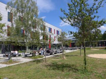Blick über die Sitzbänke vor der Cafeteria auf das Hauptgebäude des Campus Kiepenheuerallee