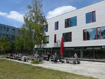 Blick über die Sitzbänke vor der Cafeteria auf das Hauptgebäude des Campus Kiepenheuerallee